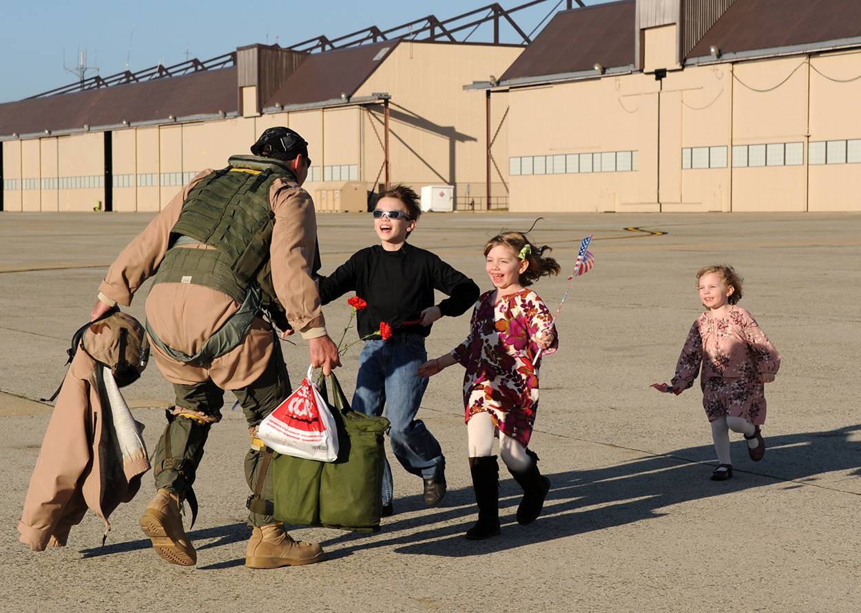 Military service member reunites with children after deployment on an airfield.